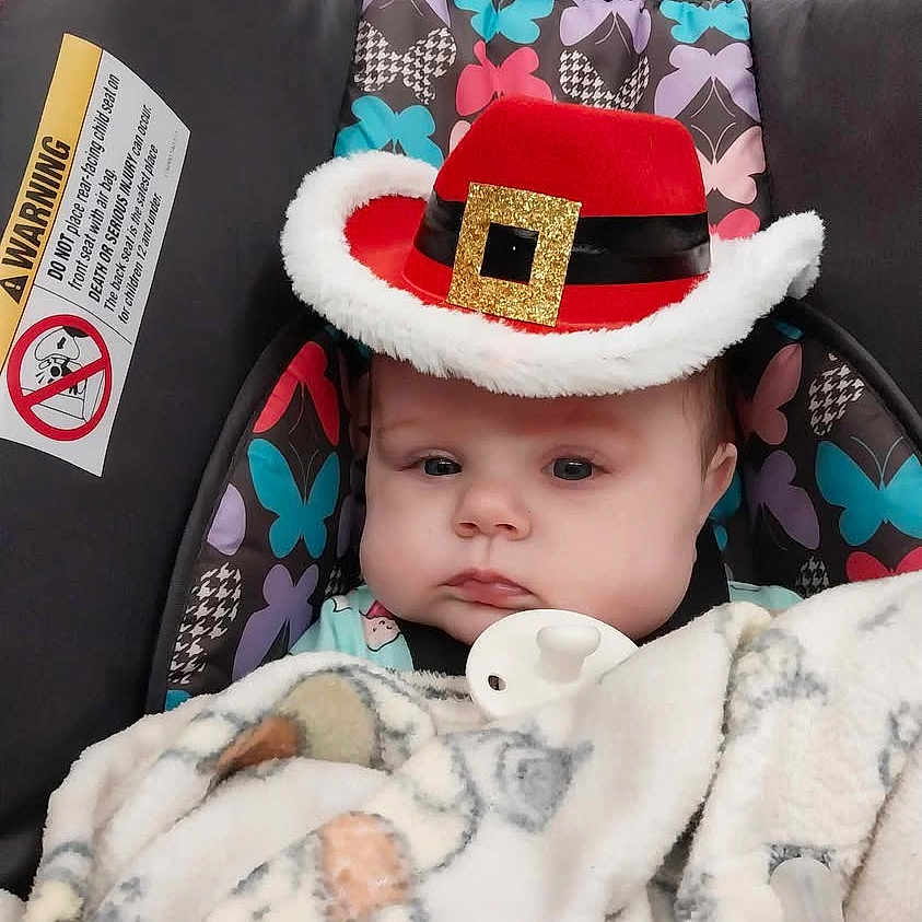 Starla is registered to the contest to win money with this photo: baby, baby_accessory, blanket, butterfly_pattern, car_seat, child, clothing, cute, expressionless, face, hat, headwear, indoor, infant, pacifier, person, red_hat, retail_store, seat_belt, winter_wear