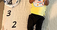 Dakota Haile is registered to the contest to win money with this photo: baby, infant, child, portrait, lying_down, bottle, drinking, bib, yellow_shirt, black_pants, gold_shoes, milestone_blanket, months, numbered_blanket, indoor, bed, textile, facial_expression, overhead_view, family_photography
