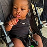 Dakota Haile is registered to the contest to win money with this photo: baby, child, infant, stroller, portrait, face, curly_hair, black_clothing, fist, hand, sitting, outdoor, sunlight, toy, harness, buckle, legs, curious, candid, person