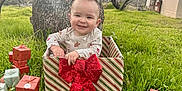 Hayes joined the competition — help win amazing prizes! baby, child, gift_box, present, red_bow, grass, tree, outdoor, smile, holiday, celebration, wrapped_gifts, nature, greenery, cute, festive, park, happy, person, daylight