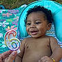 baby, child, smiling, curly_hair, birthday_candle, number_6_candle, diaper, bracelet, baby_seat, blanket, outdoor, grass, hand, person, happy, celebration, colorful, cute, infant, portrait