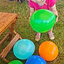 Sasha joined the competition — help win amazing prizes! toddler, balloon, green_balloon, orange_balloon, blue_balloon, yellow_balloon, grass, outdoor, child, person, pink_clothing, shoes, wooden_table, adult, legs, camping_chair, propane_tank, firewood, wheelbarrow, play