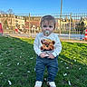 toddler, child, pacifier, grass, jeans, sneakers, sweatshirt, teddy_bear, outdoor, daylight, fence, park, people, blue_sky, trees, buildings, casual_clothing, cute, standing, sunny