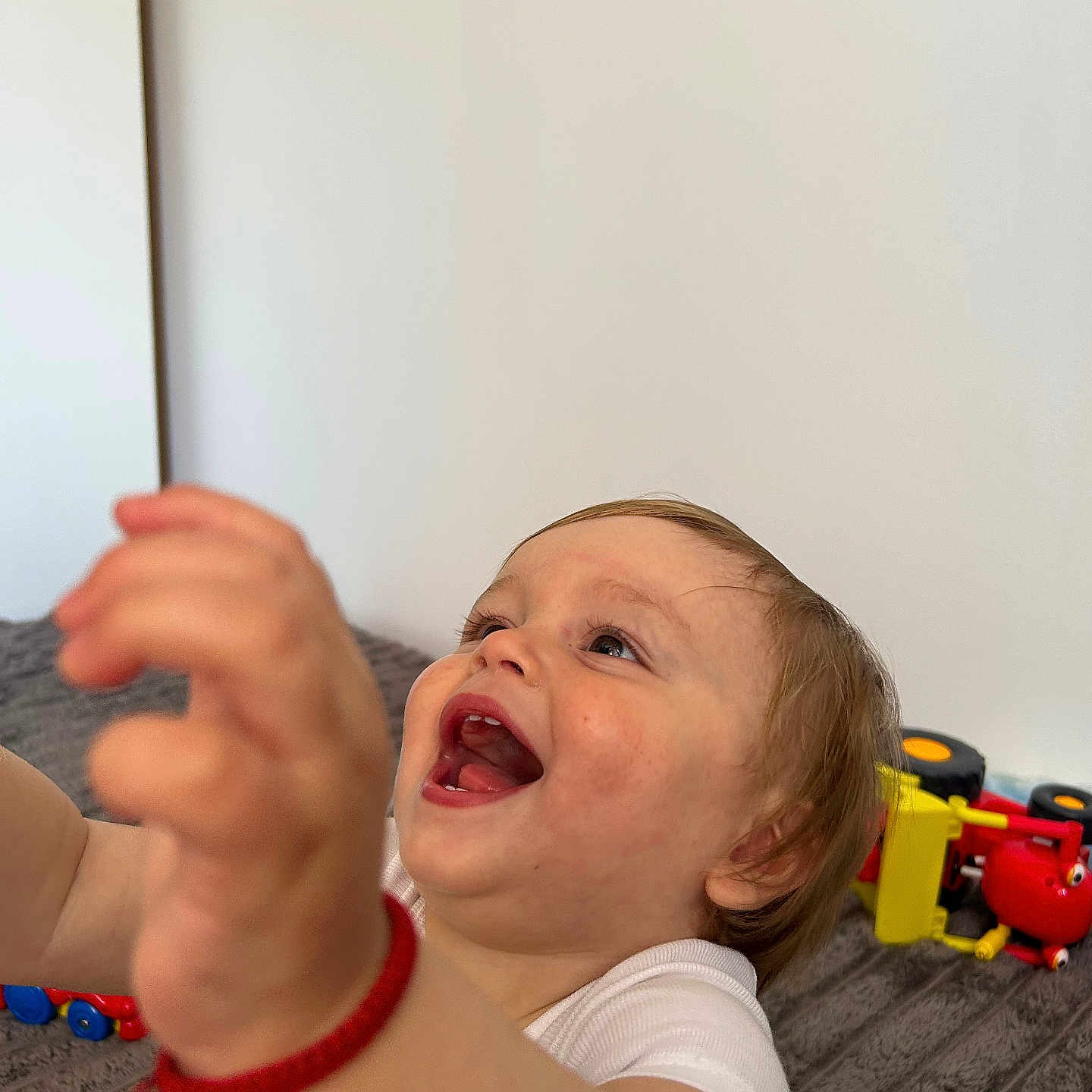 Liam Creciun participe au concours pour gagner de l'argent avec cette photo : toddler, child, happy, smiling, reaching, red_bracelet, white_shirt, toy, colorful, playtime, indoor, face, expression, person, young_child, brown_hair, cheerful, closeup, candid, joy