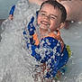 child, smiling, water, splash, life_jacket, play, happy, outdoor, summer, pool, water_sport, fun, person, blue, orange, sitting, wet, joy, closeup, face