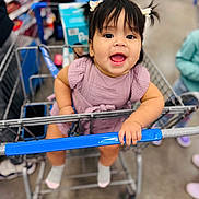 Alaia joined the competition — help win amazing prizes! child, toddler, shopping_cart, store, aisle, smiling, happy, girl, pigtails, dress, purple_clothing, socks, indoor, retail, baby, hand, face, person, floor, blurred_background