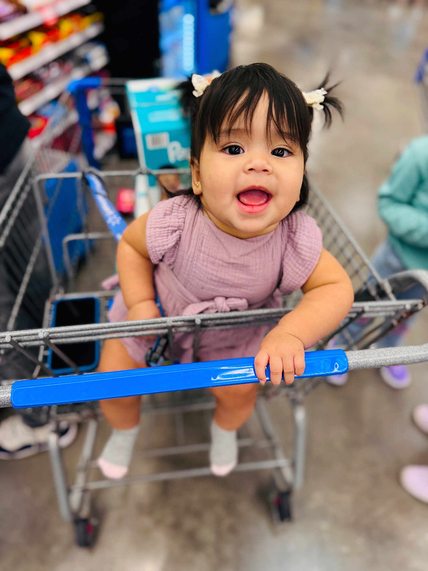 Alaia joined the competition — help win amazing prizes! child, toddler, shopping_cart, store, aisle, smiling, happy, girl, pigtails, dress, purple_clothing, socks, indoor, retail, baby, hand, face, person, floor, blurred_background