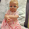 baby, child, pink_dress, cherry_pattern, hands, face, blue_eyes, blonde_hair, medical_table, paper_cover, curious, innocent, sitting, portrait, cute, infant, clothing, skin, expression, young