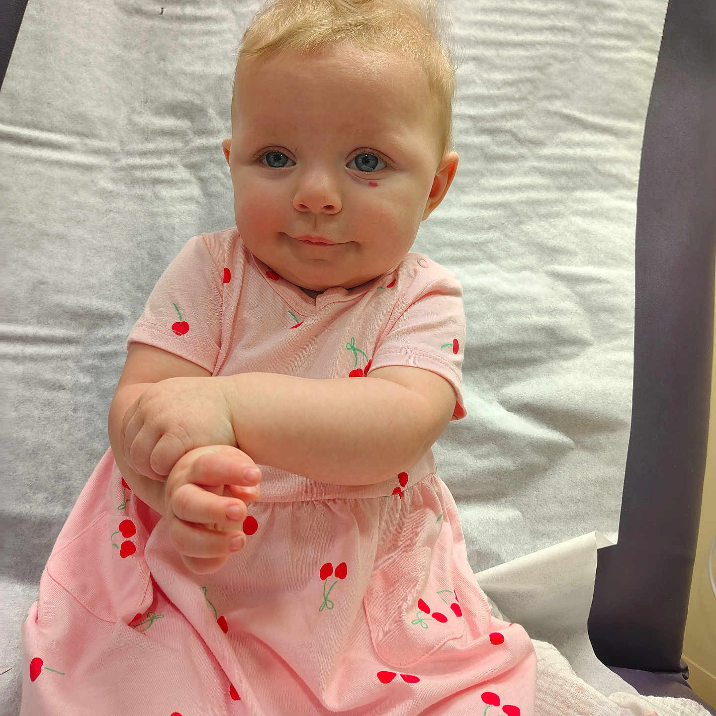 Alice joined the competition — help win amazing prizes! baby, child, pink_dress, cherry_pattern, hands, face, blue_eyes, blonde_hair, medical_table, paper_cover, curious, innocent, sitting, portrait, cute, infant, clothing, skin, expression, young