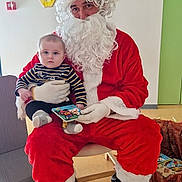 Owen a rejoint le concours — aidez-le/la à gagner de superbes lots ! baby, santa_claus, child, holiday, costume, indoor, book, person, red_clothing, beard, gloves, boots, chair, floor, wall, clock, toy, decorations, striped_clothing, smile