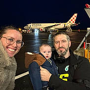 Owen a rejoint le concours — aidez-le/la à gagner de superbes lots ! airplane, airport, baby, beard, coat, family, glasses, happy, headphones, jacket, luggage_cart, man, night, outdoor, people, smile, stairs, tarmac, travel, woman