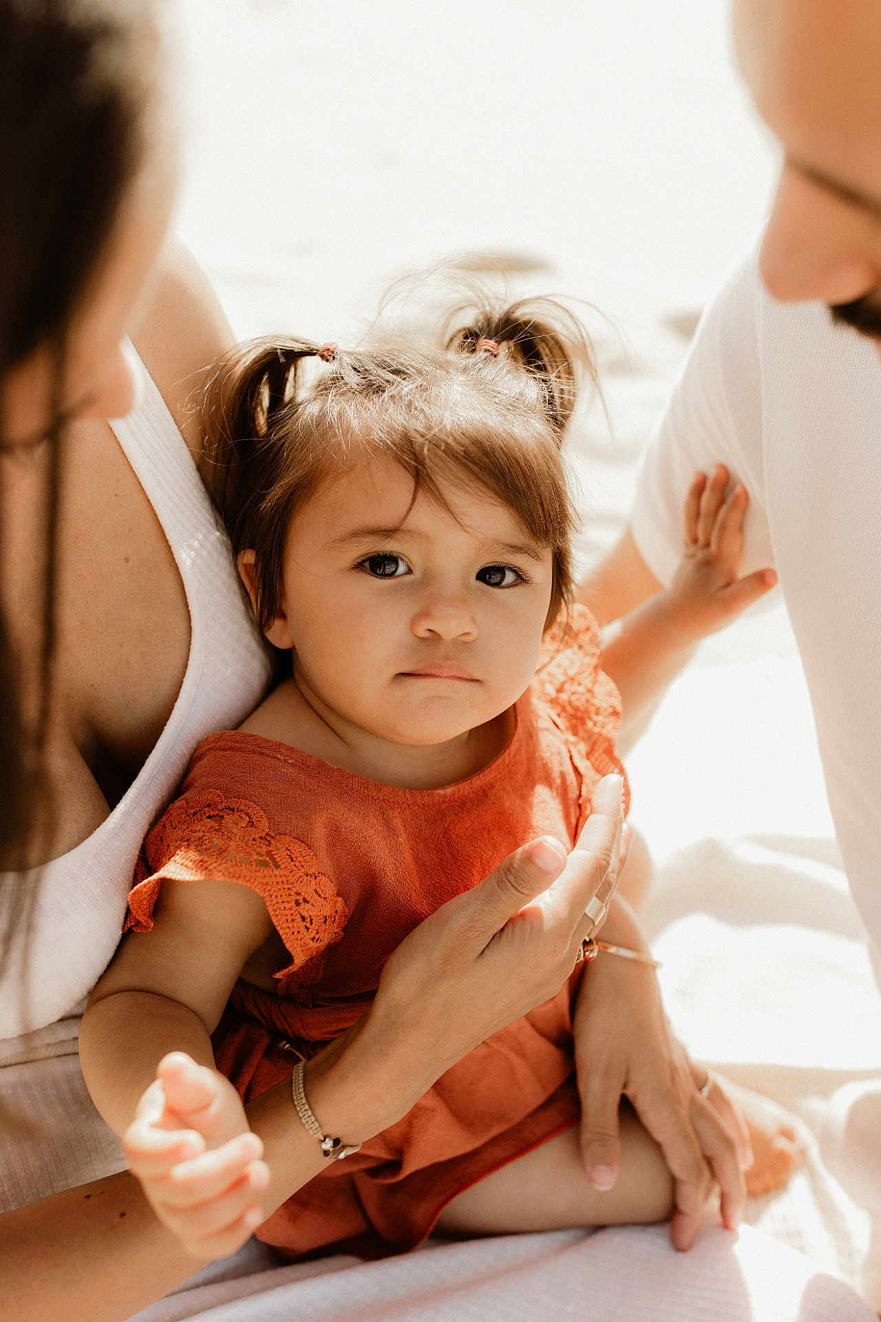 Solena a rejoint le concours — aidez-le/la à gagner de superbes lots ! toddler, child, family, adult, woman, man, orange_dress, pigtails, hands, close_up, outdoor, sunlight, skin, portrait, caring, love, gentle, expression, warm_light, sitting