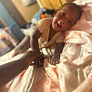 Zechariah is registered to the contest to win money with this photo: baby, bed, blanket, child, close_up, comfort, curious, expression, face, hand, indoor, infant, lying_down, pastel_colors, person, reaching, sleepwear, soft_lighting, toy, young_child
