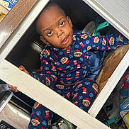 Zechariah joined the competition — help win amazing prizes! child, toddler, pajamas, bear_pattern, cabinet, cupboard, kitchen, hiding, curious, playful, sitting, face, eyes, expression, shoe, toy, stainless_steel, wooden_frame, cozy, clutter