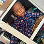 child, toddler, pajamas, bear_pattern, cabinet, cupboard, kitchen, hiding, curious, playful, sitting, face, eyes, expression, shoe, toy, stainless_steel, wooden_frame, cozy, clutter