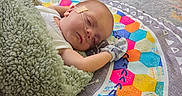 Silver is registered to the contest to win money with this photo: baby, sleeping, blanket, play_mat, colorful, indoor, glove, nasal_tube, floor, carpet, toy, child, infant, resting, cozy, patterned, cute, person, peaceful, lying_down