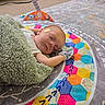 baby, sleeping, blanket, play_mat, colorful, indoor, glove, nasal_tube, floor, carpet, toy, child, infant, resting, cozy, patterned, cute, person, peaceful, lying_down