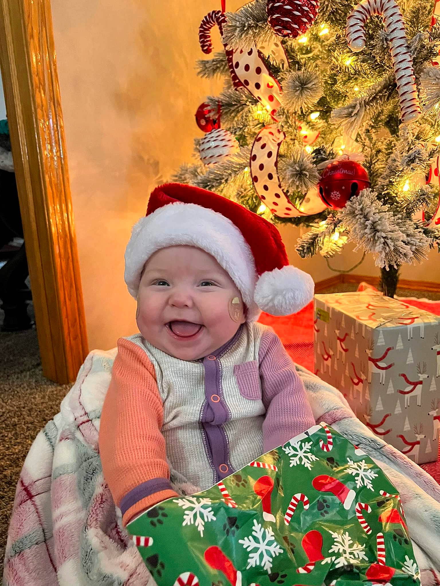 Evie is registered to the contest to win money with this photo: baby_toddler_clothing, child, christmas, christmas_decoration, christmas_eve, christmas_ornament, christmas_tree, event, happy, headwear, holiday, human_body, joy, ornament, outerwear, person, red, sleeve, smile, toddler