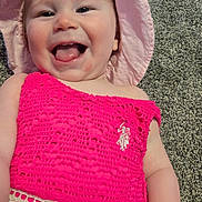 Charlotte is registered to the contest to win money with this photo: baby, child, infant, smiling, tongue_out, pink_hat, pink_dress, crochet, carpet, cheeks, face, eyes, mouth_open, happy, joyful, portrait, close_up, lying_down, home_interior, clothing