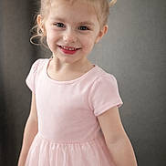 Arabella is registered to the contest to win money with this photo: child, girl, smiling, pink_dress, pigtails, blonde_hair, blue_eyes, portrait, indoor, soft_lighting, neutral_background, standing, short_sleeves, candid, cute, young_child, face, cheerful, closeup, studio_like