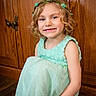 casual, child, curly_hair, cute, dress, fair_hair, floor, flower_crown, girl, green_dress, happy, headband, indoor, natural_light, person, portrait, sitting, smiling, wooden_cabinet, young_child