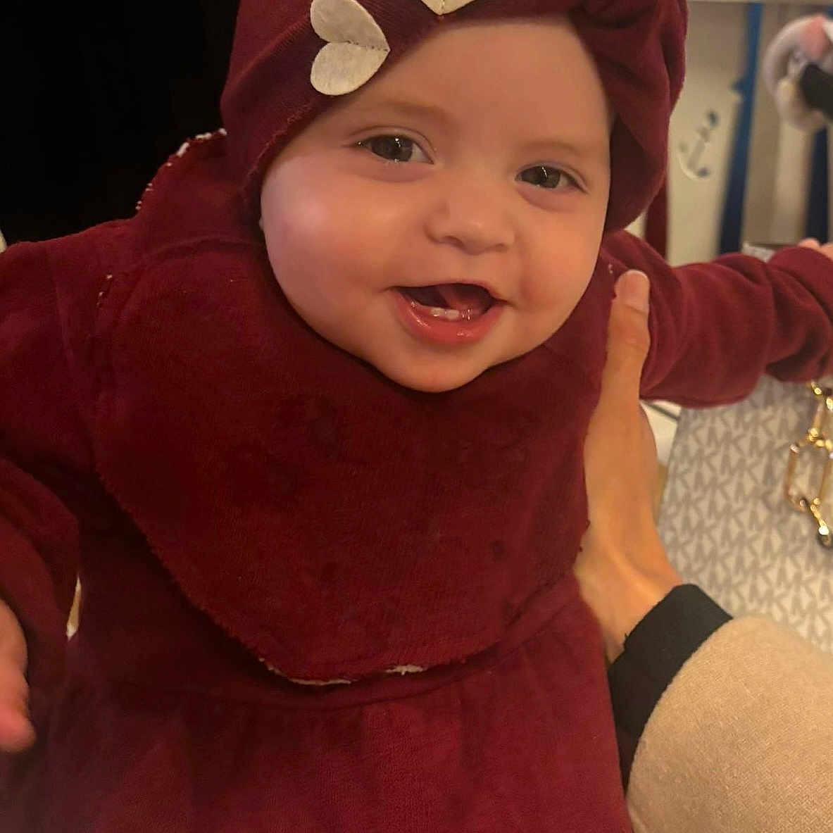 Louna a rejoint le concours — aidez-le/la à gagner de superbes lots ! adult_hand, baby, child, closeup, cute, fabric, face, hand, happy, headwrap, heart_shapes, holding, indoor, infant, maroon_clothing, patterned_bag, person, portrait, smiling, warm_clothing