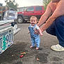 baby, child, man, overalls, denim, wrench, car, license_plate, street, vehicle, red_truck, smile, happy, barefoot, person, outdoor, asphalt, tool, supporting_hand, daylight