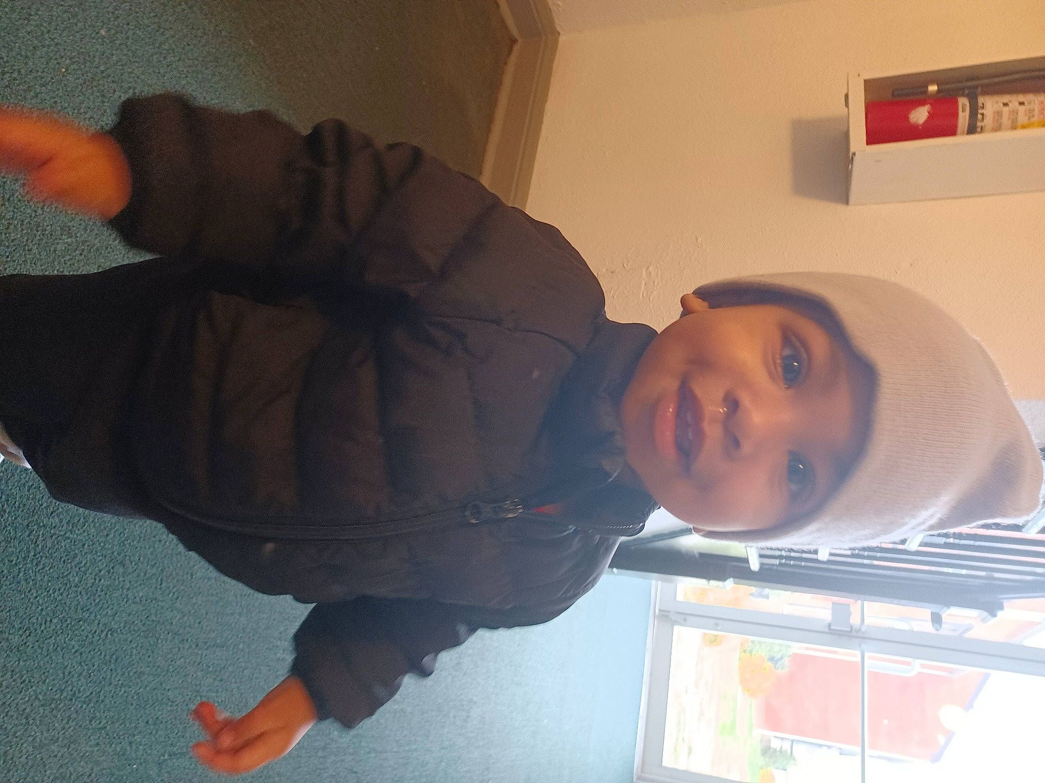 David is registered to the contest to win money with this photo: baby, child, comfort, elbow, flooring, fun, gesture, headwear, house, human_leg, jacket, knee, nose, orange, person, room, sitting, sleeve, smile, thumb