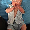 baby, infant, child, portrait, lying_down, blue_bedding, bed, floral_pattern, striped_fabric, clothing, shirt, shorts, barefoot, hands, fists, face, eyes, looking_at_camera, indoors, cozy