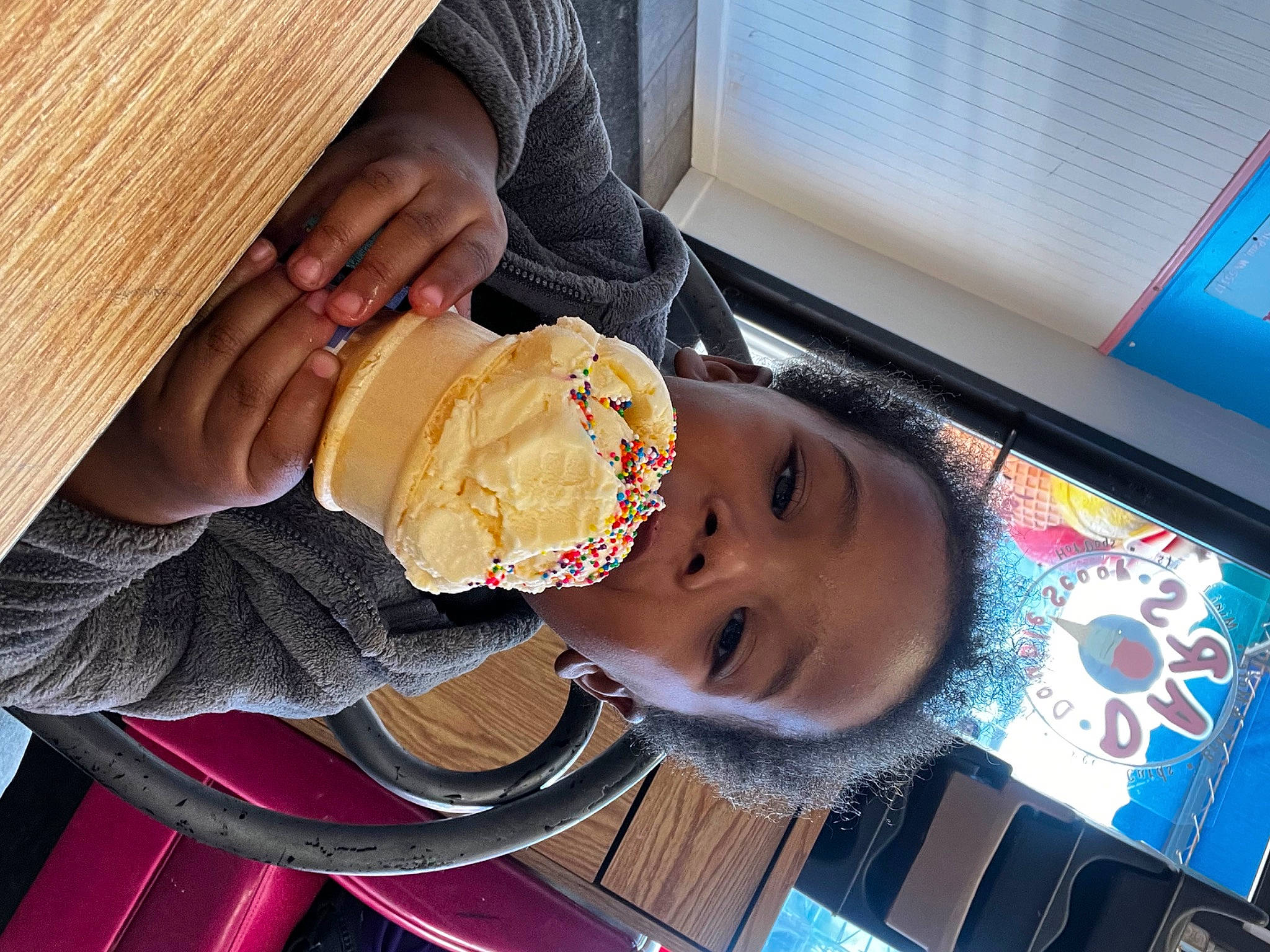 King is registered to the contest to win money with this photo: chair, child, comfort_food, cuisine, display_device, eyewear, fashion_accessory, fast_food, finger_food, food, hat, junk_food, pastry, person, plate, smile, sun_hat, tableware, toddler, wood