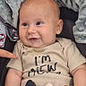 baby, infant, child, smiling, face, eyes, shirt, text, blanket, soft_texture, hand, pointing_finger, cute, skin, person, indoors, closeup, portrait, seated, cozy