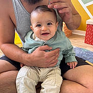 Leeroy a rejoint le concours — aidez-le/la à gagner de superbes lots ! baby, man, smile, indoor, child, holding, sitting, clothing, pants, tank_top, beard, floor, carpet, hand, face, person, room, wall, love, family