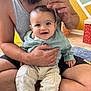 baby, man, smile, indoor, child, holding, sitting, clothing, pants, tank_top, beard, floor, carpet, hand, face, person, room, wall, love, family