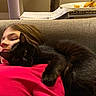 child, black_cat, couch, indoor, snuggling, red_shirt, relaxing, pet, animal, furniture, home, cozy, face, resting, cute, domestic_cat, young, comfort, leisure, warm