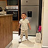 Mateo is registered to the contest to win money with this photo: child, toddler, boy, standing, walking, portrait, kitchen, refrigerator, appliances, home, indoor, clothing, white_shirt, striped_pants, sneakers, fashion, floor, wooden_cabinets, safe, family_photo