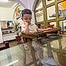 Mateo is registered to the contest to win money with this photo: child, toddler, boy, portrait, seated, high_chair, restaurant, indoors, table, wooden_furniture, tablet, smartphone, white_shoes, curly_hair, thoughtful, face, hand_on_cheek, cuba_sign, glass_door, flowers