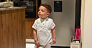 Mateo joined the competition — help win amazing prizes! child, boy, toddler, portrait, standing, walking, indoors, kitchen, refrigerator, oven, microwave, wooden_cabinets, white_shirt, striped_pants, sneakers, fashion, curly_hair, facial_expression, home, wine_box