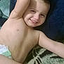 child, toddler, smiling, diaper, bare_chest, lying_down, blanket, hair_spiked, happy, relaxed, indoor, person, young_child, skin, face, arm, gesture, comfort, candid, casual
