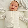 baby, infant, white_clothing, heart_pattern, sweater, pants, lying_down, soft_surface, cute, face, eyes, buttoned_sweater, child, portrait, indoors, young_child, comfort, expression, small, person