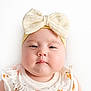 baby, infant, portrait, headband, bow, chubby_cheeks, close_up, white_background, onesie, cute, soft_skin, studio_light, neutral_expression, face, eyes, adorable, baby_clothing, fruit_print, round_face, sleepy_look