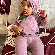 Jordan is registered to the contest to win money with this photo: baby, child, infant, purple_clothing, hat, bracelet, sitting, blanket, pattern, indoor, cute, portrait, knitwear, expression, person, young_child, cozy, soft_texture, curious, wide_eyes