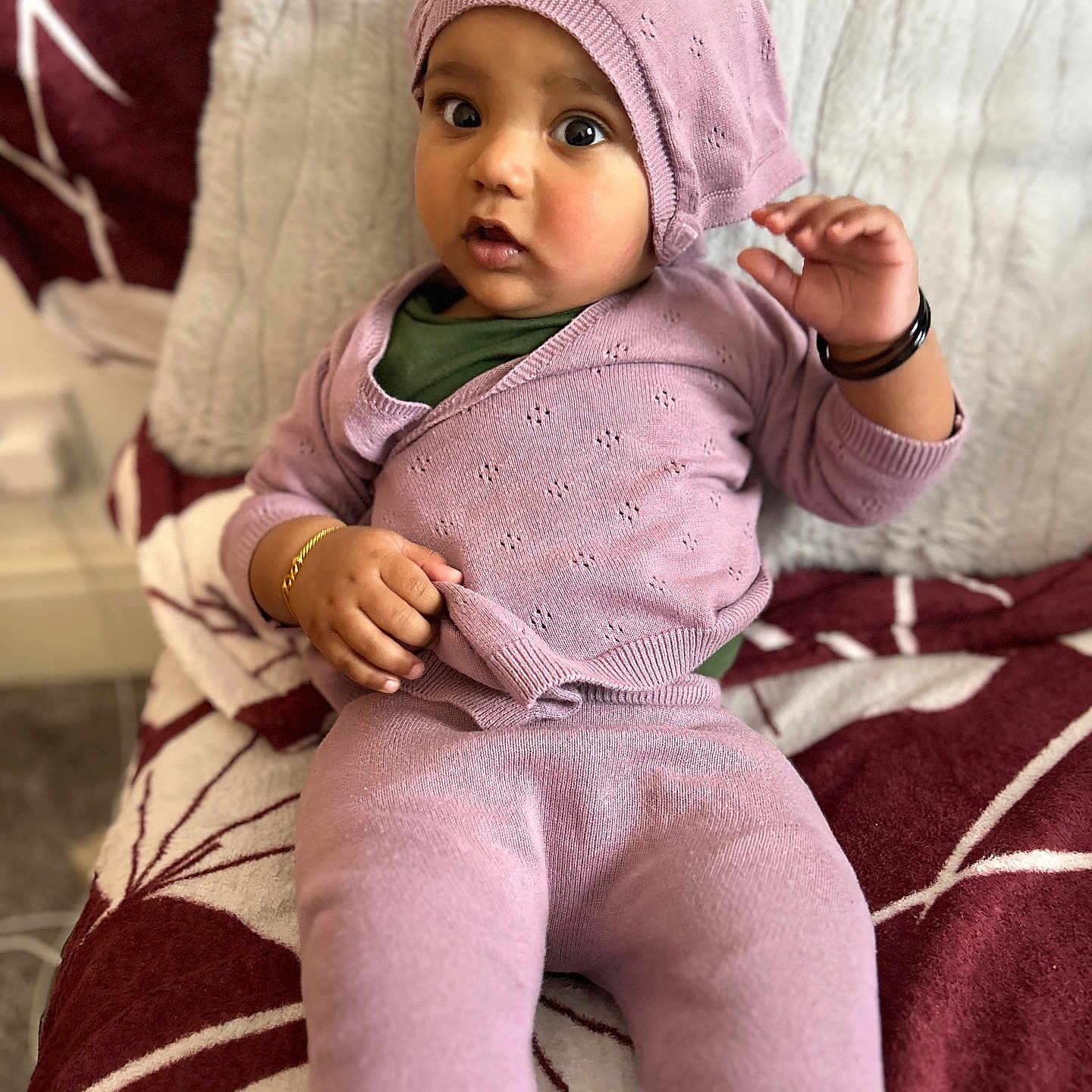 Jordan is registered to the contest to win money with this photo: baby, blanket, bracelet, child, cozy, curious, cute, expression, hat, indoor, infant, knitwear, pattern, person, portrait, purple_clothing, sitting, soft_texture, wide_eyes, young_child