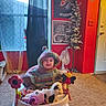 Amitalyriea is registered to the contest to win money with this photo: baby, walker, plush_toy, cow_toy, pink_toy, knit_hoodie, carpet, fan, window, curtain, poster, artificial_tree, door, red_wall, floor, child, indoor, smiling, toy, person