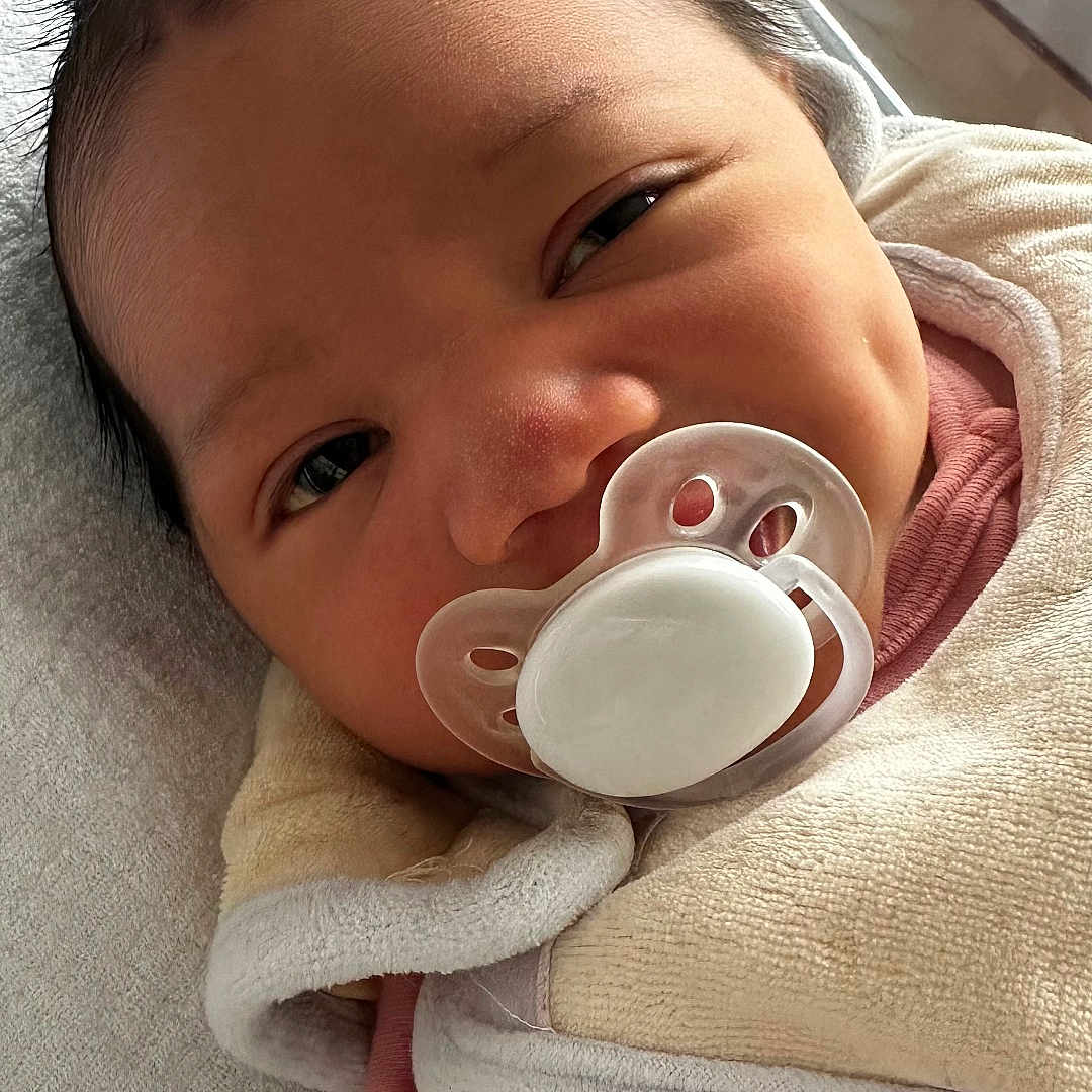 élora a rejoint le concours — aidez-le/la à gagner de superbes lots ! baby, blanket, closeup, cozy, cute, eyelashes, face, head, indoors, infant, newborn, pacifier, person, pink_clothing, portrait, resting, skin, sleeping_area, soft_texture, young_child