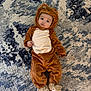 Michael is registered to the contest to win money with this photo: baby, child, costume, lion, animal_outfit, carpet, floor, cute, infant, face, portrait, clothing, footwear, lying_down, indoor, expression, looking, adorable, soft_texture, young