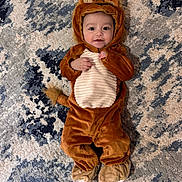 Michael joined the competition — help win amazing prizes! baby, child, costume, lion, animal_outfit, cute, smiling, lying_down, carpet, rug, brown, beige, blue, patterned, face, infant, clothing, footwear, hand, portrait