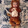 baby, child, costume, lion, animal_outfit, cute, smiling, lying_down, carpet, rug, brown, beige, blue, patterned, face, infant, clothing, footwear, hand, portrait