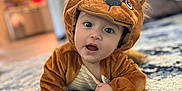 Michael is registered to the contest to win money with this photo: baby, child, costume, lion_costume, cute, indoor, carpet, rug, plush, living_room, furniture, curious, portrait, crawling, soft_lighting, expression, animal_costume, home, hand, face