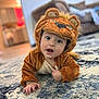 baby, child, costume, lion_costume, cute, indoor, carpet, rug, plush, living_room, furniture, curious, portrait, crawling, soft_lighting, expression, animal_costume, home, hand, face