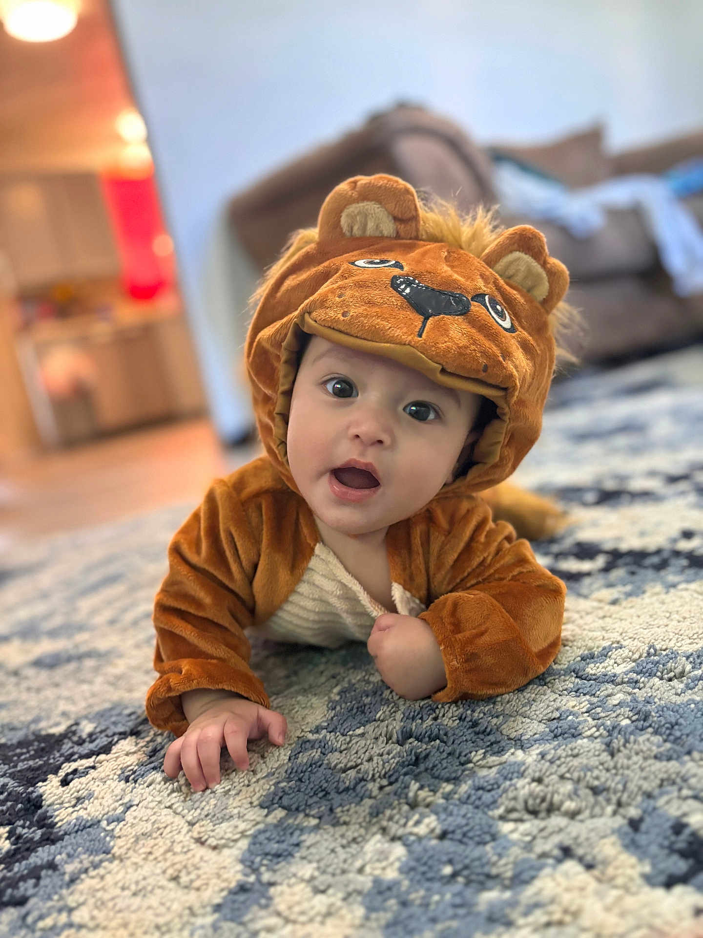Michael is registered to the contest to win money with this photo: baby, child, costume, lion_costume, cute, indoor, carpet, rug, plush, living_room, furniture, curious, portrait, crawling, soft_lighting, expression, animal_costume, home, hand, face